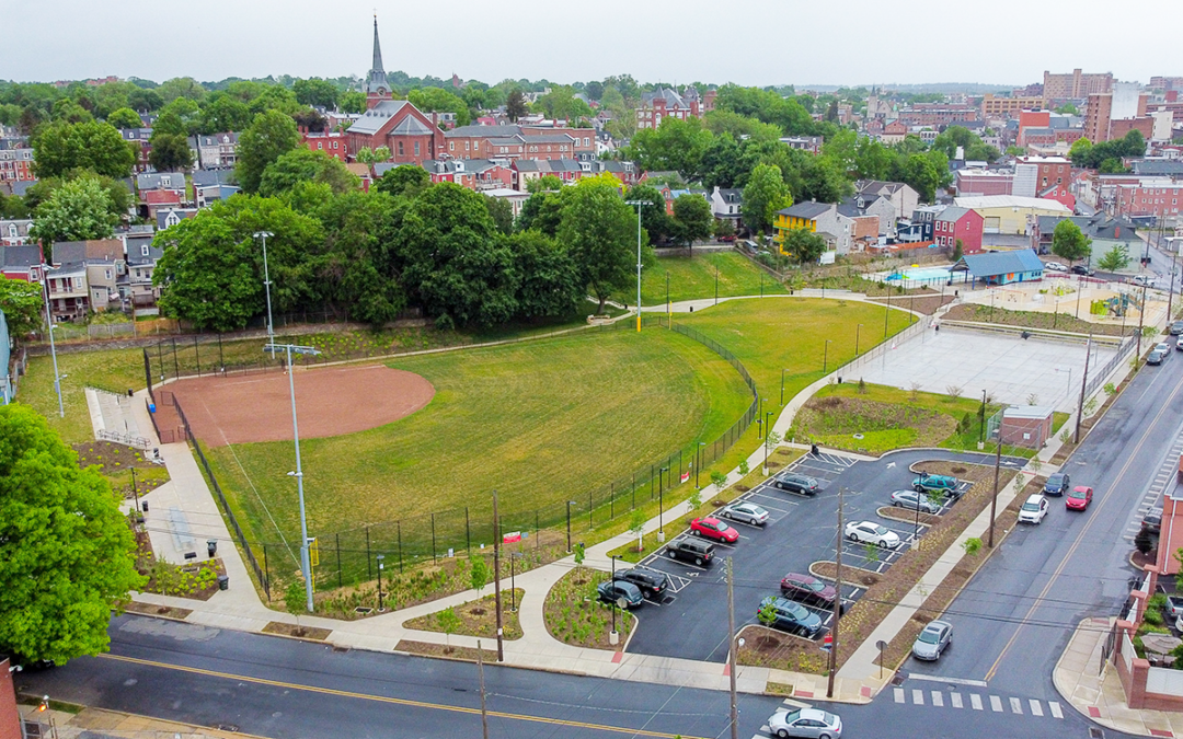 drone view of lush green baseball field sitting in front of residential properties in urban environment with church steeple in back