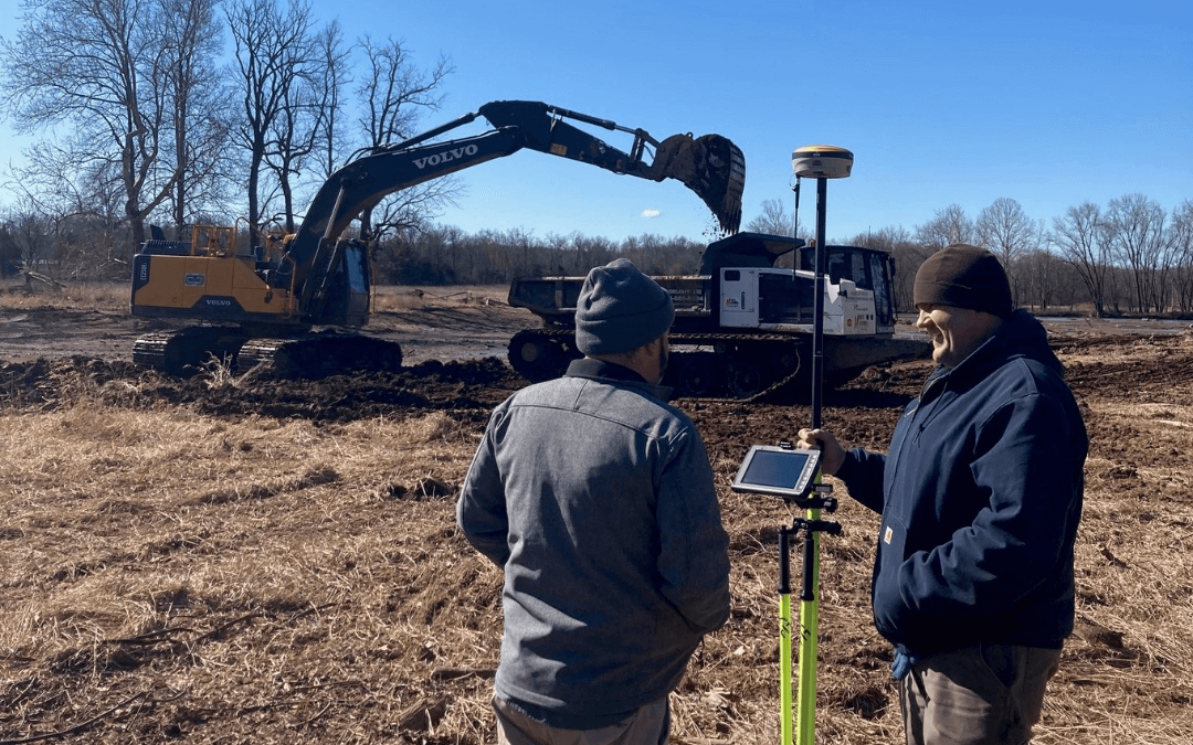 two flyway employees standing in front of excavation equipment on a job site with blue sky in the background